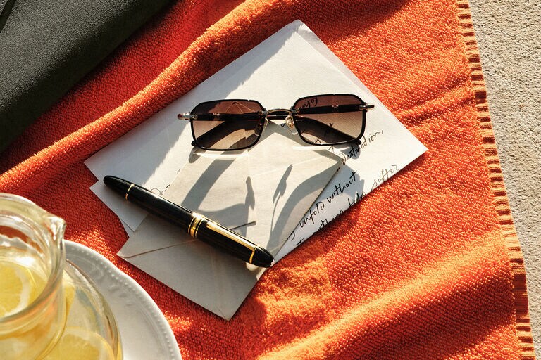 Montblanc fountain pen in black precious resin with gold-coated accents, beside sunglasses and an open letter on a vibrant orange towel.
